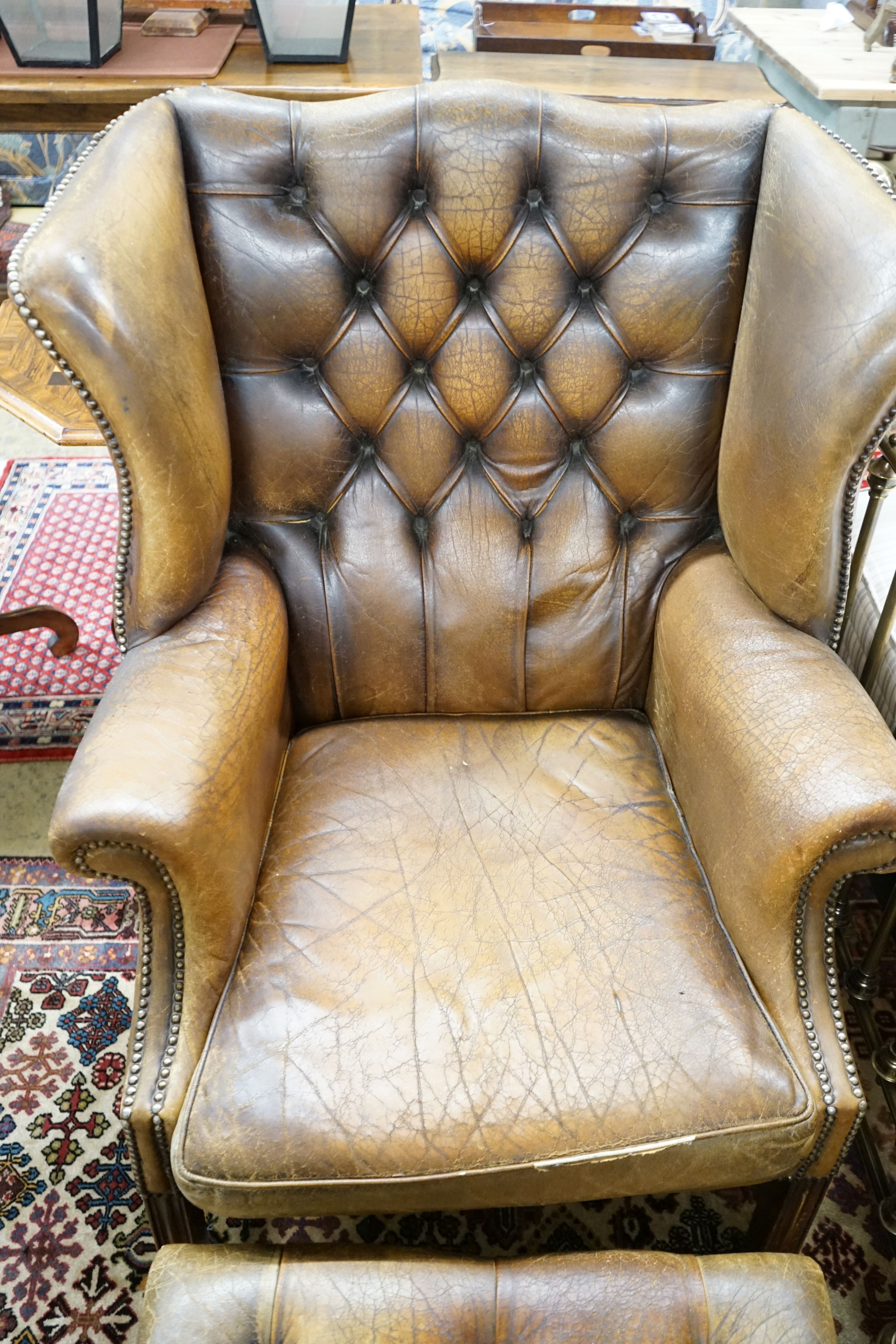 A leather wing armchair upholstered in buttoned brown leather, width 82cm, depth 77cm, height 110cm together with a similar foot stool